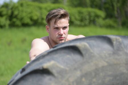 Tire and man with muscles and serious face, on green trees background, selective focusの写真素材