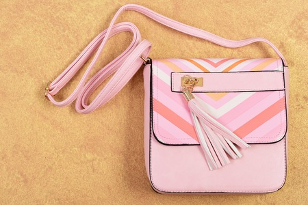 Accessory in modern style made of leather. Shopping and fashion design concept. Purse in light pink color with stripes. Handbag for women on orange texture background, top viewの写真素材