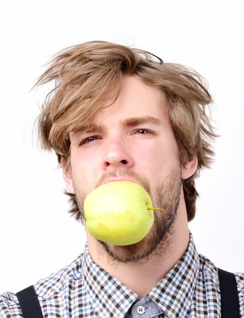 Slim shape and healthy diet concept. Farmer with fresh fruit in mouth, isolated on white background. Idea of proper nutrition. Man with beard and stylish hairdo bites green apple, close upの写真素材
