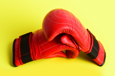 Bright red mittens for boxing lying on each other isolated on yellow background, concept of fight and sportive competitionの写真素材