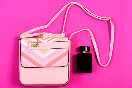 Accessories in modern style isolated on magenta pink background. Purse in light pink color and perfume. Handbag for women and black bottle of scent, top view. Fashion and glamour conceptの写真素材