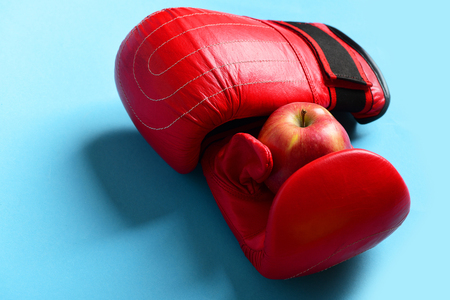Sport equipment and fruit on bright blue background. Boxing gloves in red color. Pair of leather boxing sportswear with juicy red apple. Knock out and healthy nutrition conceptの写真素材