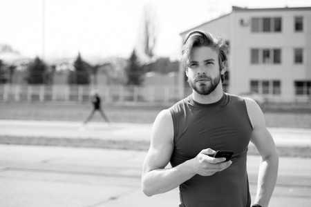 summer activity and sport. healthy lifestyle and communication, athletic bearded man or sexy handsome guy with muscular body holds mobile or cell phone training sunny outdoor, black and whiteの写真素材