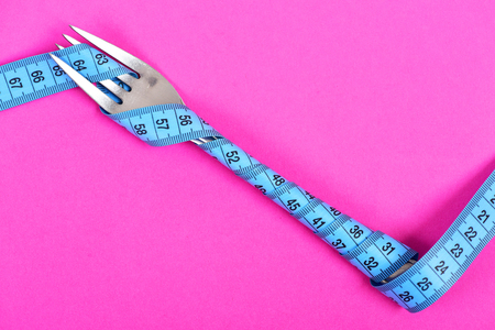Traditional metal fork wrapped neatly with turquoise blue measuring tape on light pink background, copy space. Concept of dieting and fit shapeの写真素材