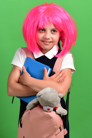 School girl with smiling face isolated on green background. Girl holds blue book and teddy bear.の写真素材