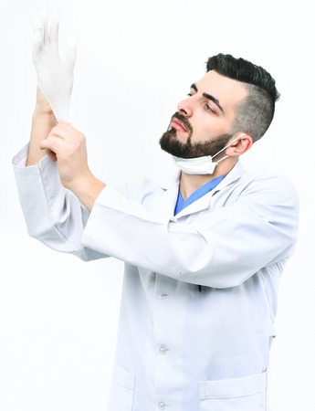 Surgeon with beard puts glove on. Medicine and professional skills concept. Physician isolated on white background. Man with serious face in laboratory coat.の写真素材