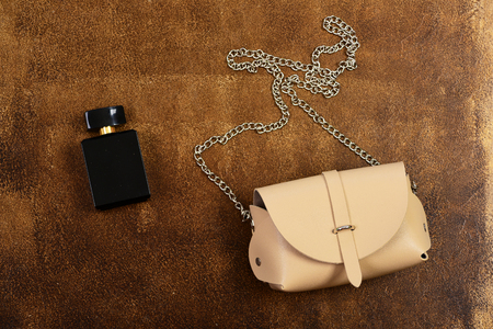 Leather purse and perfume bottle on brown suede background. Female accessories, close up. Beige handbag with long metal chain. Fashion and scent conceptの写真素材