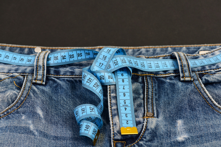Healthy lifestyle and dieting concept. Close up of jeans with measure tape around waist.  Top part...