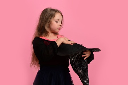 Child in witch costume and black hat. Halloween and costume party concept. Girl holds big witch cone...