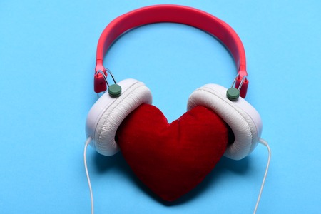 Leisure, music and Valentines day concept. Headset for music and love symbol. Modern and stylish earphones isolated on cyan background, close up. Headphones in white and red color with soft toy heartの写真素材
