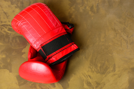 Boxing gloves in red color. Knock out and strong boxers punch concept. Pair of leather boxing sportswear. Sport equipment on dark beige suede backgroundの写真素材