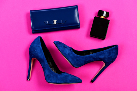 Accessories in formal style for women isolated on pink background, top view. Clutch and female footwear with bottle of scent. Fashion and style concept. Purse and shoes in dark blue color with perfumeの写真素材
