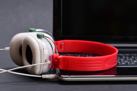 Headphones and black laptop. Music and digital equipment concept. Earphones in red and white colors...