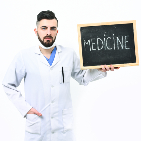 Doctor with beard holds little blackboard with word medicine written on it. Man with serious face in white medical gown isolated on white background. Treatment, recovery and ambulance services conceptの写真素材