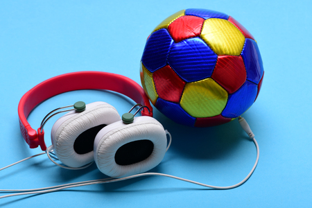 Modern earphones and football on turquoise background. Headphones in white and red color with colorful soccer ball. Music and sports equipment concept. Headset for music placed on ballの写真素材