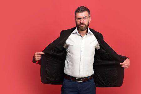 Guy with open jacket and notebook. Man in classic outfit with beard holds red book. Businessman with confident face and glasses isolated on red background. Success, business and studying conceptの写真素材