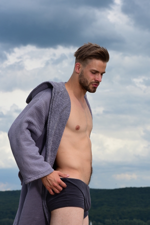 Male model posing against the sky. Bearded attractive guy enjoy healthy morning. Adult handsome man in fashionable bathrobe. Morning concept. Sexy young macho on the sky.の写真素材