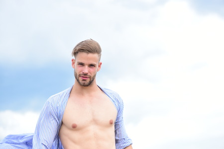 Morning concept. Sexy young macho on the sky. Bearded attractive guy enjoy healthy morning. Adult handsome man in fashionable shirt. Male model posing against the sky.の写真素材