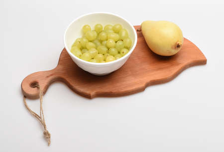 Leaf shaped wooden board isolated on white background. Juicy grapes and ripe yellow pear on cutting board. Cooking and healthy food concept. Delicious summer fruit, close up.の写真素材