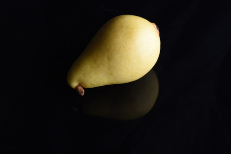 Art and healthy food concept. Juicy ripe yellow pear on black background.Delicious summer fruit, close up. Fruit reflection on black surface.の写真素材