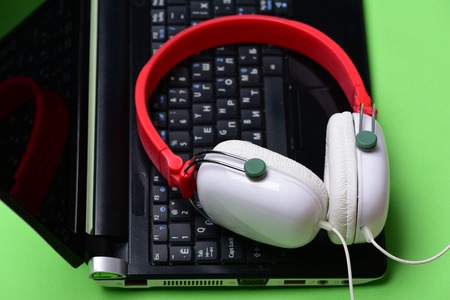 Music and digital equipment concept. Electronics on light green background. Headphones and black laptop. Sound recording idea. Earphones in red and white colors made of plastic with computer.の写真素材