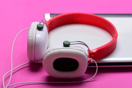 Headphones and silver laptop. Electronics isolated on magenta pink background. Earphones made of plastic with computer. Music and digital equipment concept. Sound recording idea.の写真素材