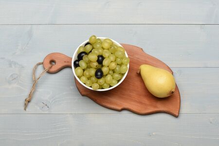 Cooking and healthy food concept. Delicious summer fruit, top view. Juicy grapes and ripe yellow pear on cutting board. Leaf shaped wooden board on vintage surface.の写真素材