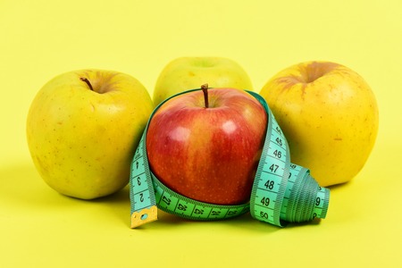 Apples of red and yellow colour wrapped with twisted cyan measuring tape isolated on yellow...