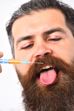 Man showing his tongue. Medicine and health concept. Bearded man with stylish haircut holds syringe near face and tries to lick it. Young man looking on needle isolated on white backgroundの写真素材