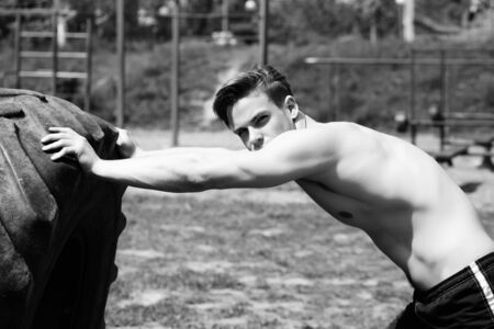 Guy with assured face and strong body pushes huge wheel at sports ground. Concept of heavy weight class sportsの写真素材
