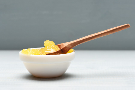 Cup of honey on grey background. Spoonful of honey in porringer, close up. Sweet natural nectar on white vintage surface, selective focus. Healthy food and lifestyle concept.の写真素材