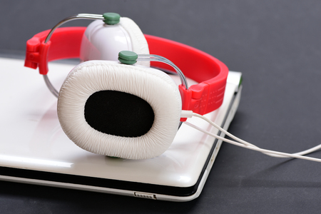 Sound recording idea. Music and digital equipment concept. Electronics on grey background. Earphones in red and white colors made of plastic with computer. Headphones and silver laptop.の写真素材