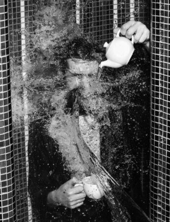 Handsome man, bearded hipster with beard and moustache in red checkered shirt wet with big splash of water washes in shower and pours tea with closed eyes on colorful mosaic backgroundの写真素材