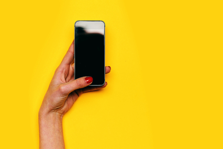 communication and technology, girl touch mobile or cell phone screen with hand, has red manicure on yellow background. internet surfing, video conferencing, copy spaceの写真素材