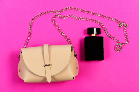 Handbag for women and black bottle of scent, top view. Accessories in modern style on magenta pink background. Fashion and style concept. Purse in light beige color and perfumeの写真素材