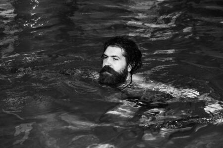 Handsome man or swimmer, bearded sexy hipster with wet beard and hair swims in pool indoors on blue water backgroundの写真素材