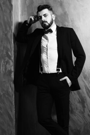 bearded man, long beard, brutal caucasian hipster with moustache in black elegant suit with bow-tie posing with serious face on brown studio wall backgroundの写真素材