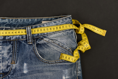 Healthy lifestyle and dieting concept. Upper part of denim trousers isolated on black background....
