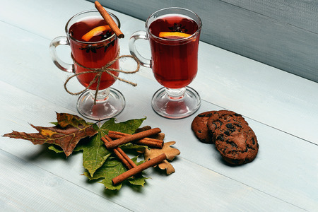 chocolate cookies with hot drink of mulled wine or tea with cinnamon spice stick in glass near green autumn leaves at christmas on grey wooden backgroundの写真素材