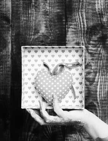 female hand smeared in golden paint or glister holding handmade pink polka dots valentine heart in present box on brown vintage studio backgroundの写真素材