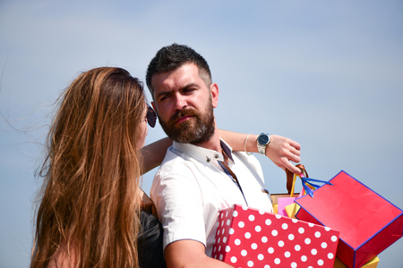 Man with beard and long haired woman hold shopping bags. Sexy girl and guy with calm faces make purchases. Couple in love carries pink packets on blue sky background. Shopping and relationship conceptの写真素材