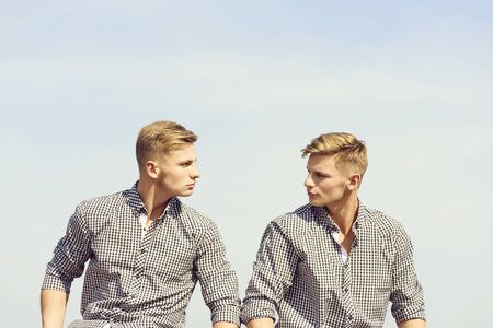 young stylish handsome twins in checkered shirts posing with serious faces on blue sky backgroundの写真素材