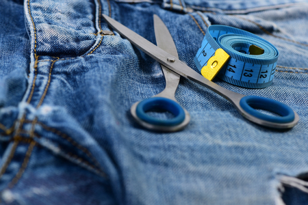 Making clothes and design concept. Metal scissors and measure tape on jeans. Jeans crotch and pocket, close up. Tailors tools on denim fabric, selective focus.の写真素材