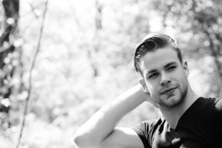Happy young man with smile, stylish haircut and facial hair stretches his neck on light park...