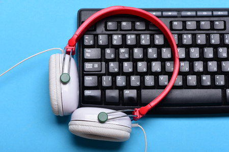 Earphones in red and white with computer keyboard. Electronic appliances on turquoise background. Headphones and black keyboard. Music and digital equipment concept. Sound recording and technologyの写真素材
