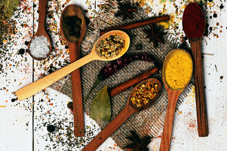set of various aromatic spices of curry powder or turmeric, paprika, salt, bay leaf, black pepper with spoons, chili pepper and cinnamon on sackcloth on vintage wooden white background, top viewの写真素材