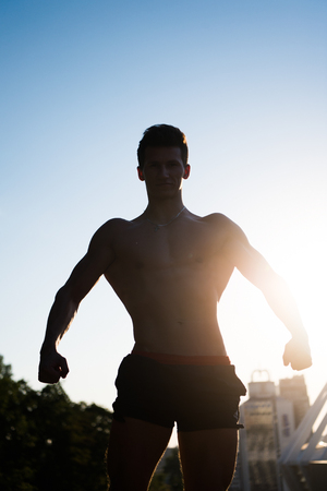 Sportsman showing muscular body, muscles, biceps, triceps on blue sky and sunlight background. Fitness and sport. Nature and healthy lifestyleの写真素材
