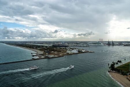 Boats floating on blue sea water with ships in port on skyline on cloudy sky background in Fort...