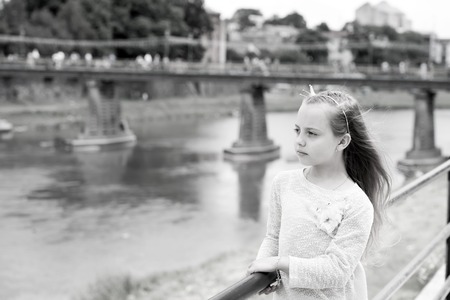 Portrait of a lovely little happy cute princess girl with long blonde curly hair at summer sunny day looking on the riverの写真素材