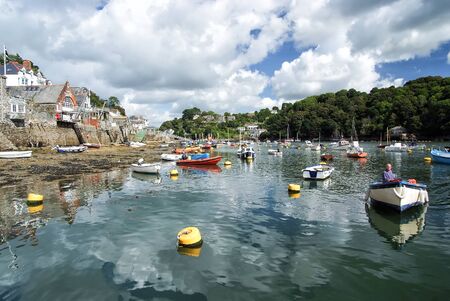 Fowey, UK - March 23, 2010: town quay, green trees at river harbor with boats on water on cloudy blue sky. Summer vacation concept. Tourism and travel destinationのeditorial素材